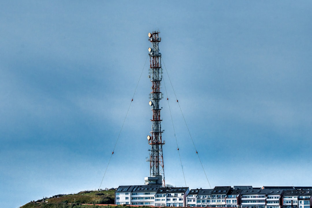 Tall communication tower stands above buildings on hill.